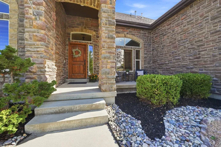 Stone facade with arched entryway, natural wood entry door, and decorative rock landscaping