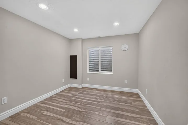 Recessed lighting, wood-finish flooring, light neutral wall paint, and a window with blinds
