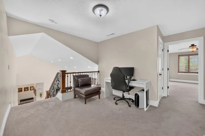 Carpeted landing with vaulted ceilings, recessed lighting, and a wood and wrought iron staircase railing