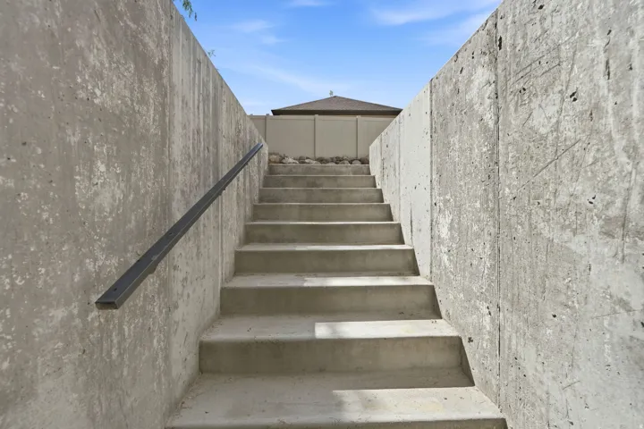 Concrete retaining walls with integrated concrete staircase and black metal handrail