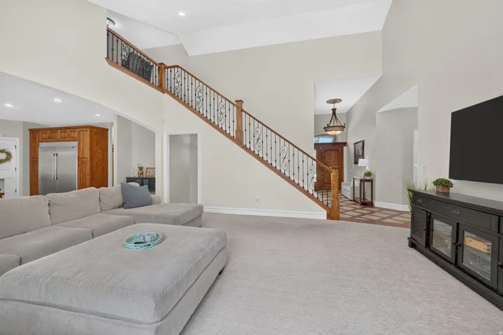 Two-story ceiling, wood staircase with ornate metal balusters, and recessed lighting