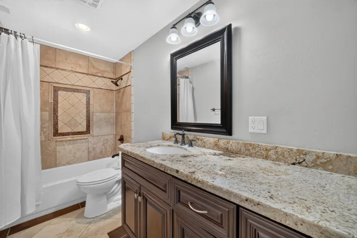 Vanity with stone countertop and integrated sink, framed mirror, and three-light fixture