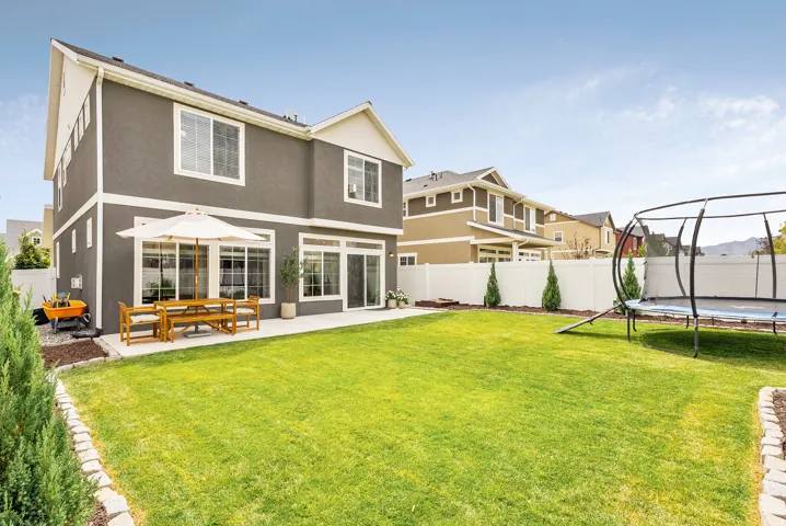 Expansive green lawn, white privacy fencing, concrete patio, sliding glass doors, and a neutral-toned stucco exterior