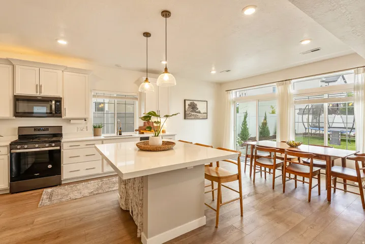 Contemporary kitchen and dining area featuring light-toned cabinetry, stainless steel appliances, a center island with countertop seating, wood-finish flooring, and a dining table with seating for six
