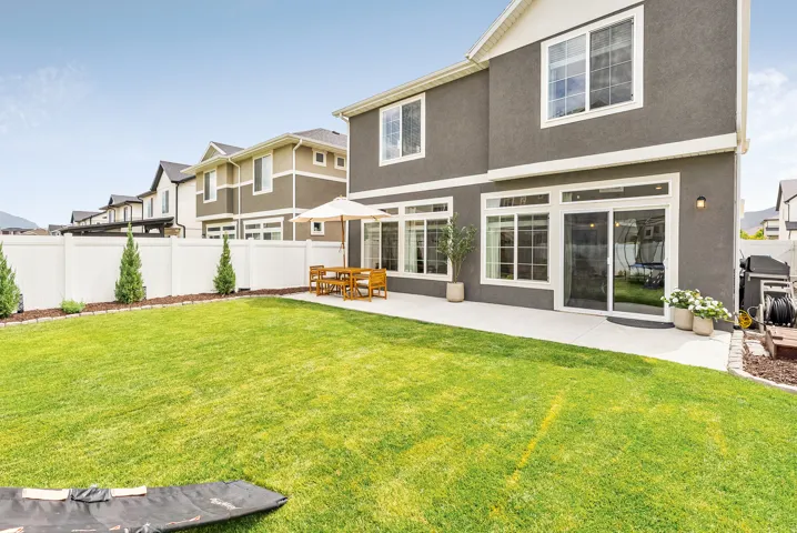 Expansive backyard with a manicured lawn, concrete patio, and white privacy fencing