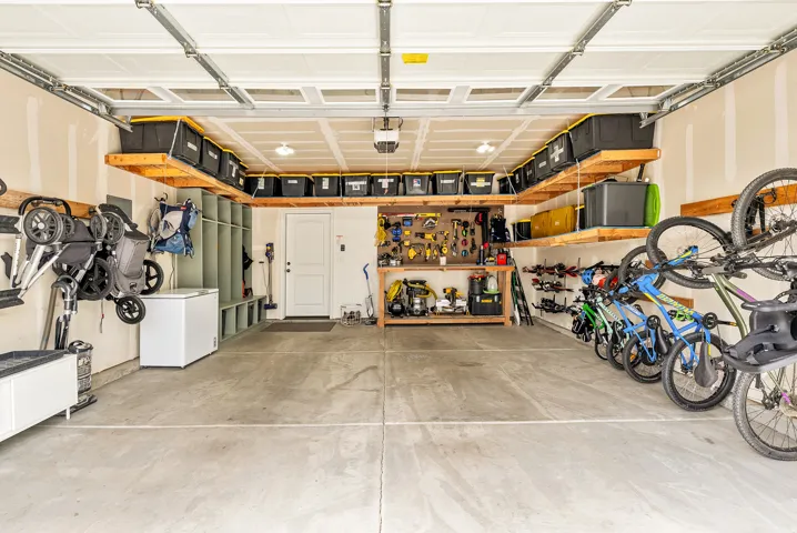 Spacious garage featuring epoxy-coated concrete flooring, custom orange wall-mounted cabinetry and shelving, recessed ceiling lighting, overhead storage systems, and ample room for multiple vehicles and recreational equipment storage