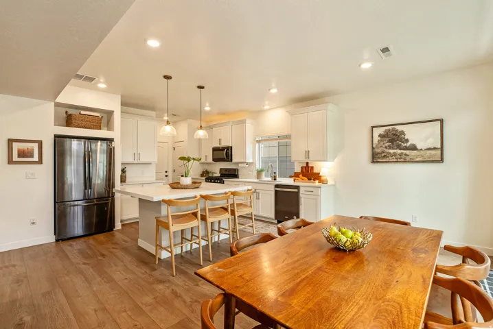 Open-concept kitchen featuring white cabinetry, stainless steel appliances, a center island with pendant lighting, and wood-finish flooring