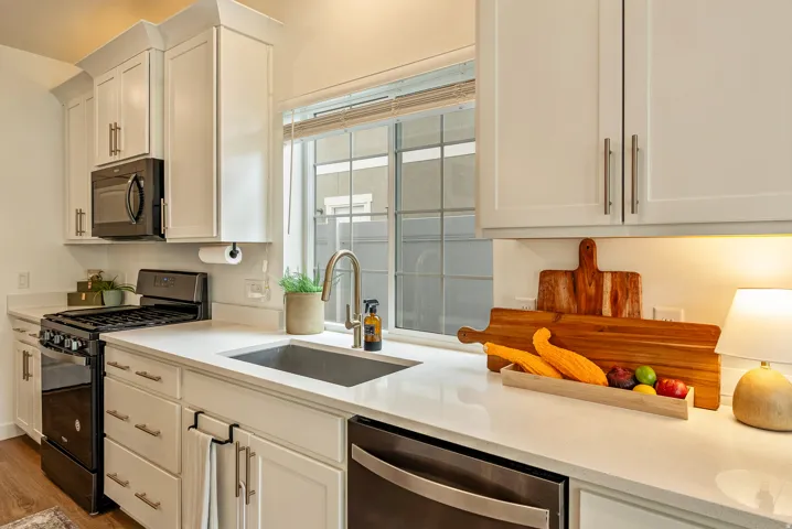 Contemporary kitchen featuring white shaker-style cabinetry with brushed nickel hardware, quartz countertops, a stainless steel undermount sink with gooseneck faucet, and black gas range