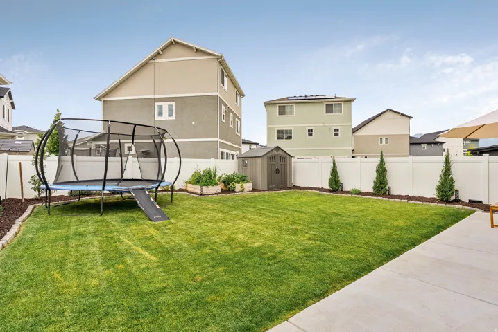 Expansive backyard featuring a manicured lawn, a white privacy fence, and a storage shed