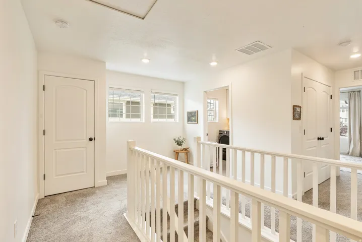 Upper landing featuring light gray carpet, white painted railings, and multiple windows