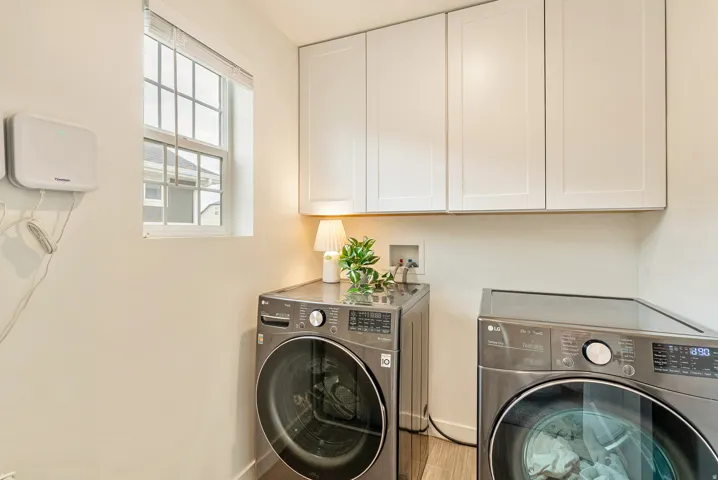 Laundry area featuring light-toned walls, white upper cabinetry, and a window with blinds