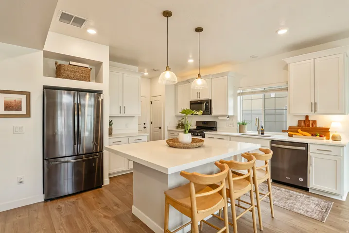 Kitchen featuring light wood-finish flooring, white cabinetry, integrated stainless steel appliances, a center island with countertop seating, and pendant lighting