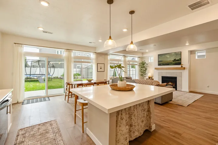 Open-concept interior with wood-finish flooring, a white quartz island, and a built-in fireplace featuring a wood mantel