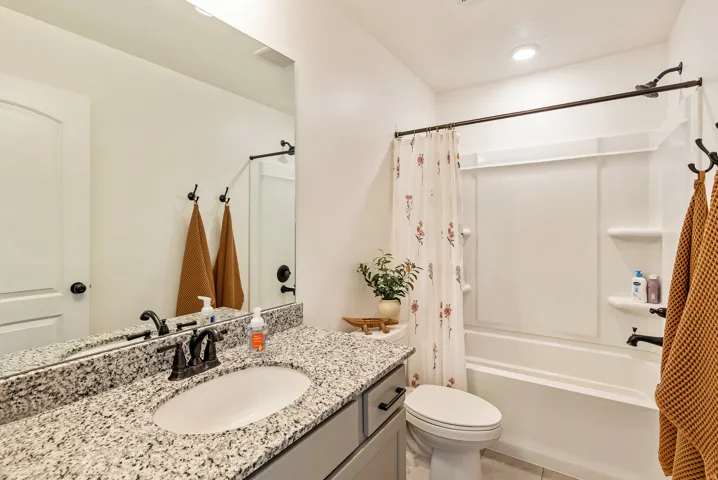 Spa-inspired bathroom featuring a granite-topped double vanity with dual vessel sinks and matte black fixtures, frameless glass shower enclosure with subway tile surround, white cabinetry with soft-close drawers, recessed lighting, and brushed nickel hard