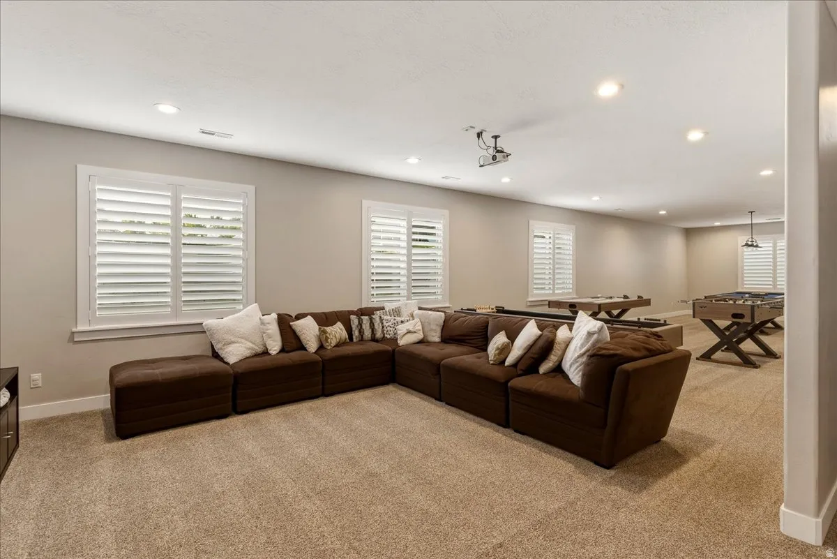 Recessed lighting, neutral wall tones, plantation shutters, and a ceiling-mounted projector create a versatile entertainment area