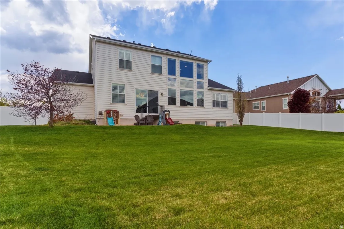 Expansive green lawn, white vinyl fencing, multi-pane windows, sliding glass door, and a mature tree