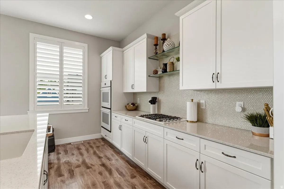 White shaker cabinetry with black hardware, wood-finish flooring, light-toned countertops, and a mosaic tile backsplash
