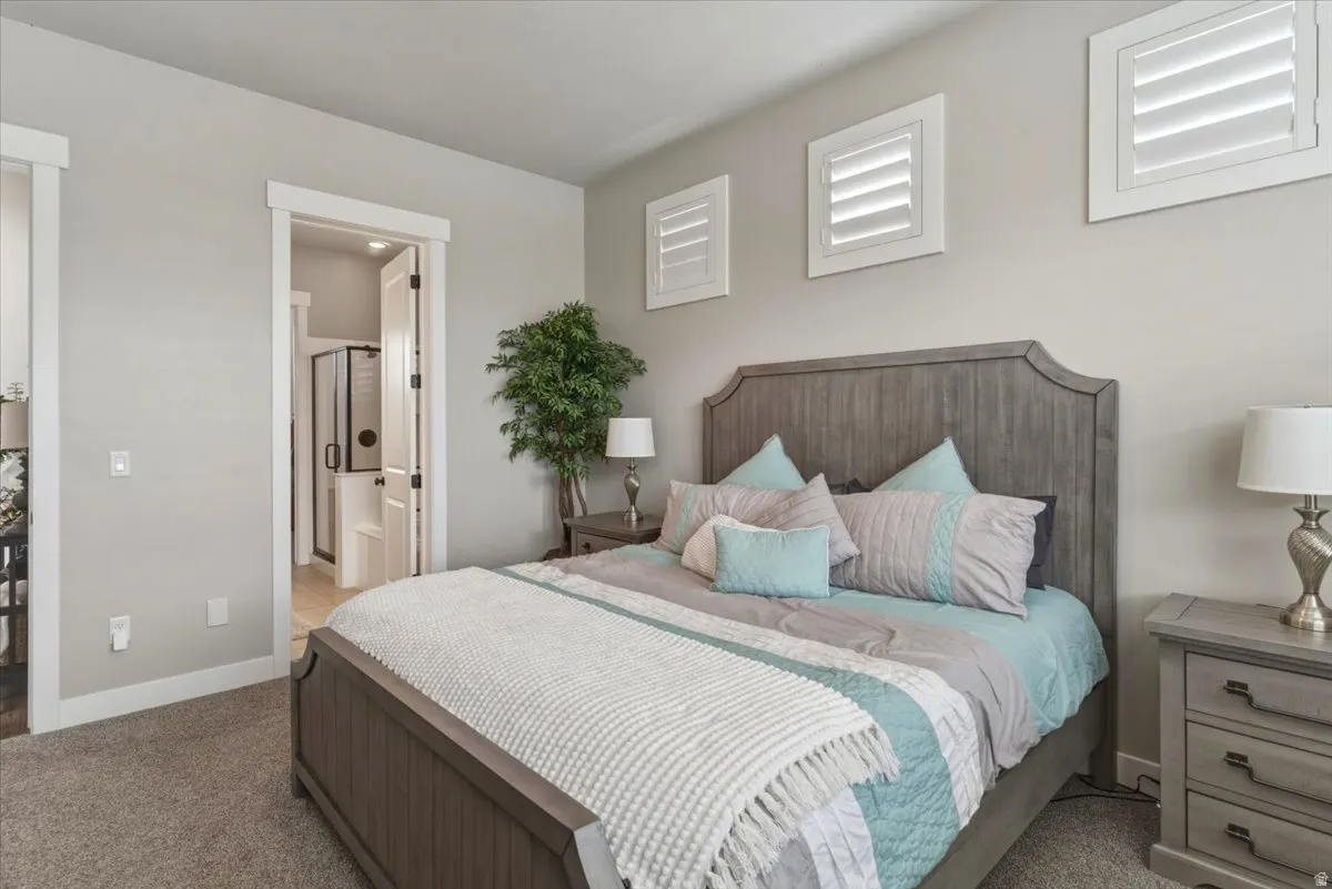 Carpeted room with a wooden bed frame, plantation shutters, and an open doorway to a bathroom with a glass-enclosed shower