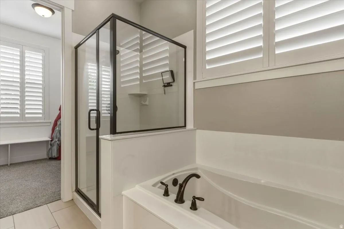 Contemporary bathroom featuring a built-in tub with dark bronze fixtures, a glass-enclosed shower, and plantation shutters