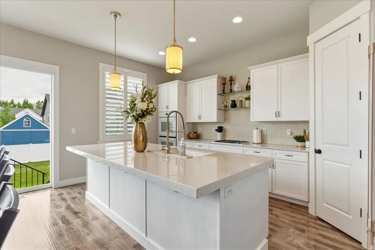 Expansive kitchen island with a light-toned countertop, white cabinetry, wood-finish flooring, recessed lighting, and a full-height tile backsplash
