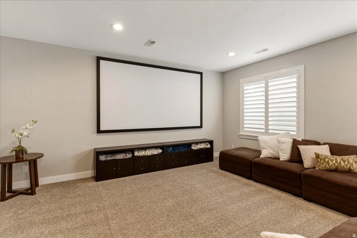 Large projection screen with a dark frame, built-in storage cabinetry, plantation shutters, recessed lighting, and carpeting