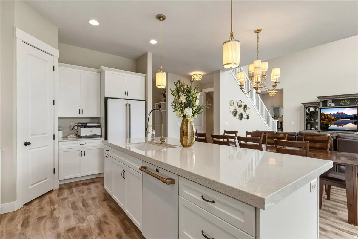 Kitchen island with a light-toned countertop and integrated sink, stainless steel appliances, white cabinetry with dark hardware, and wood-finish flooring