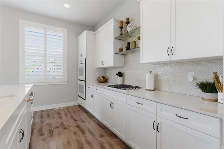 White cabinetry, solid surface countertops, wood-finish flooring, built-in double oven, and gas cooktop