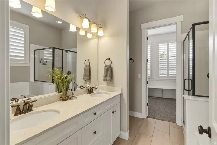 Dual vanity with undermount sinks and bronze-finish faucets, quartz-finish countertop, white cabinetry with dark hardware, and an expansive mirror