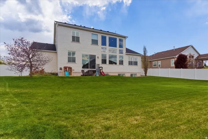 Expansive green lawn, white vinyl fencing, multi-pane windows, sliding glass door, and a mature tree
