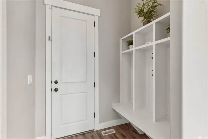 Built-in storage bench with open shelving, wood-finish flooring, white paneled door, and neutral wall color