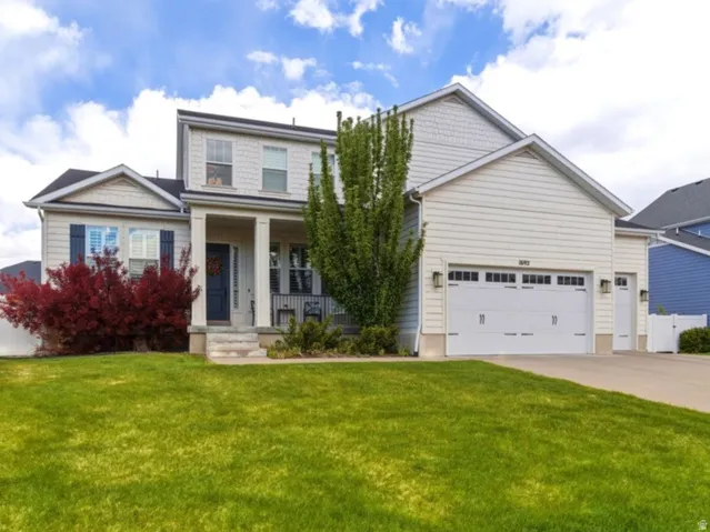 Two-story property featuring light-colored siding, a covered front porch, and a two-car garage with overhead doors