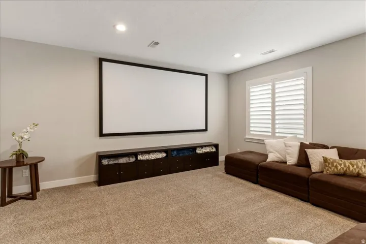 Large projection screen with a dark frame, built-in storage cabinetry, plantation shutters, recessed lighting, and carpeting