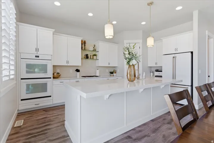 Kitchen featuring a large island, wood-finish flooring, white cabinetry, integrated double ovens, and recessed lighting