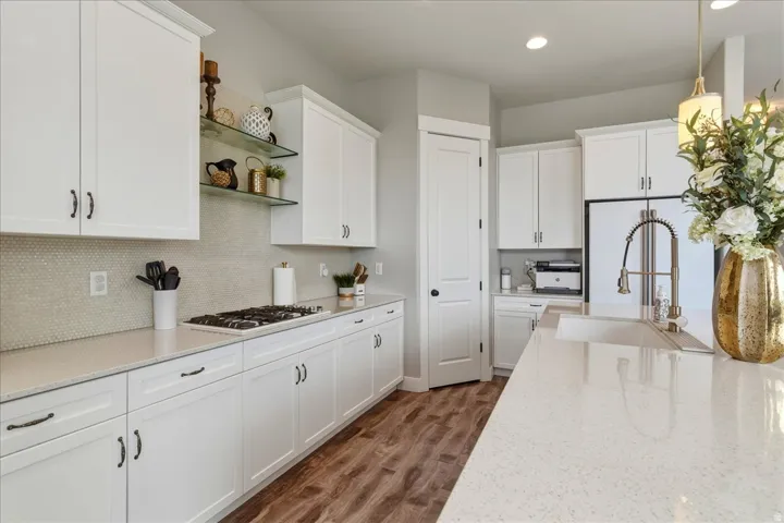 White cabinetry, light-toned countertops, wood-finish flooring, built-in gas range, and a single basin sink with a gooseneck faucet