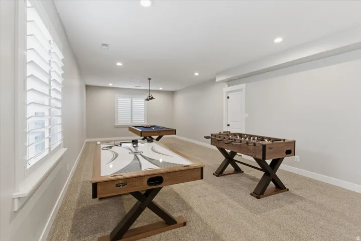 Expansive recreation room featuring two windows with white louvered shutters, recessed lighting, and light-colored carpeting