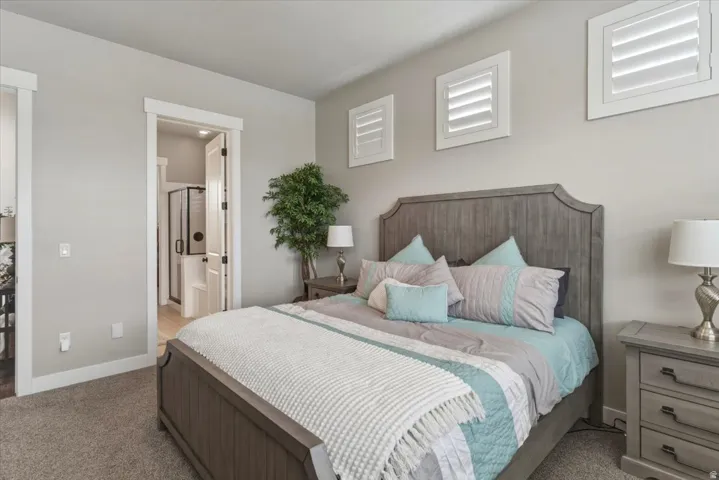 Carpeted room with a wooden bed frame, plantation shutters, and an open doorway to a bathroom with a glass-enclosed shower