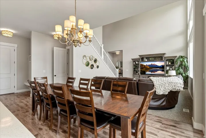 Expansive interior featuring high ceilings, wood-finish flooring, a grand chandelier, a carpeted living area, and a white staircase