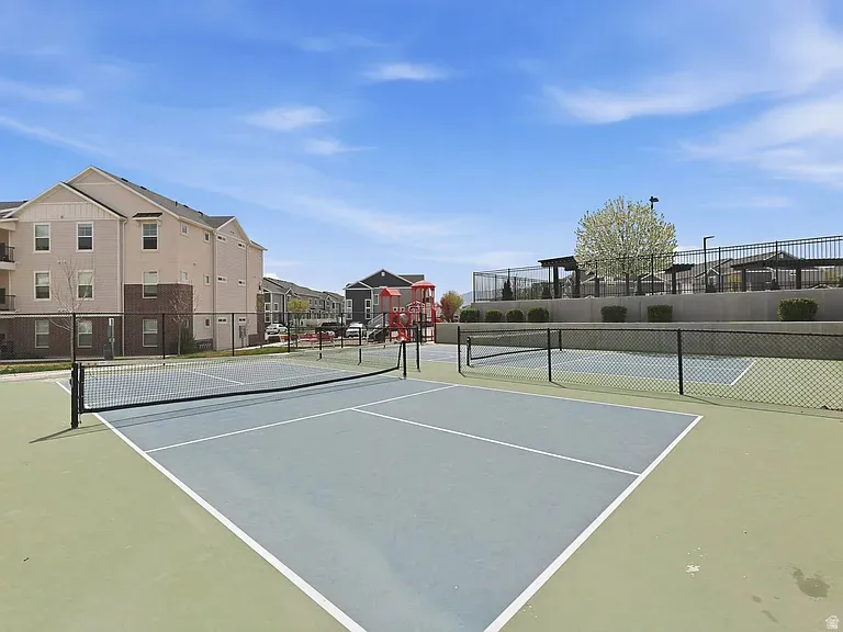 Two outdoor sports courts with perimeter fencing, a distant residential structure with balconies, and a tree with white blossoms