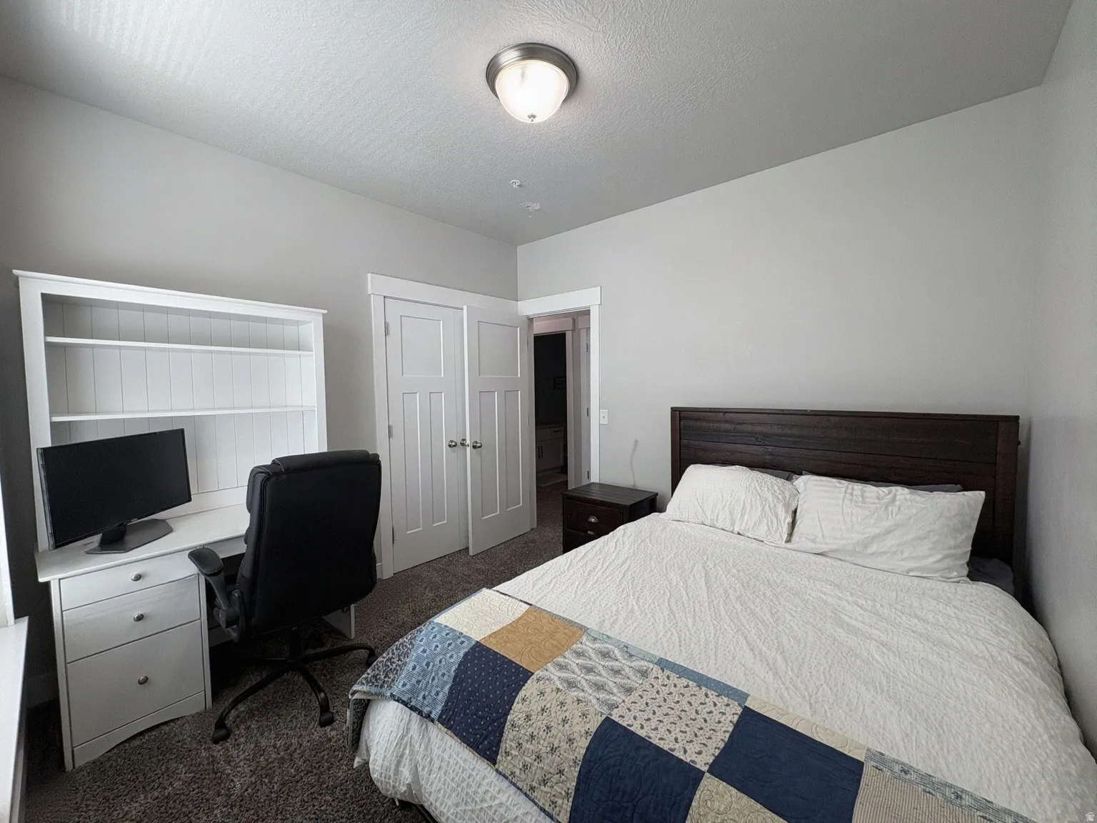 Carpeted room featuring light gray walls, a wood-finish headboard, and built-in shelving