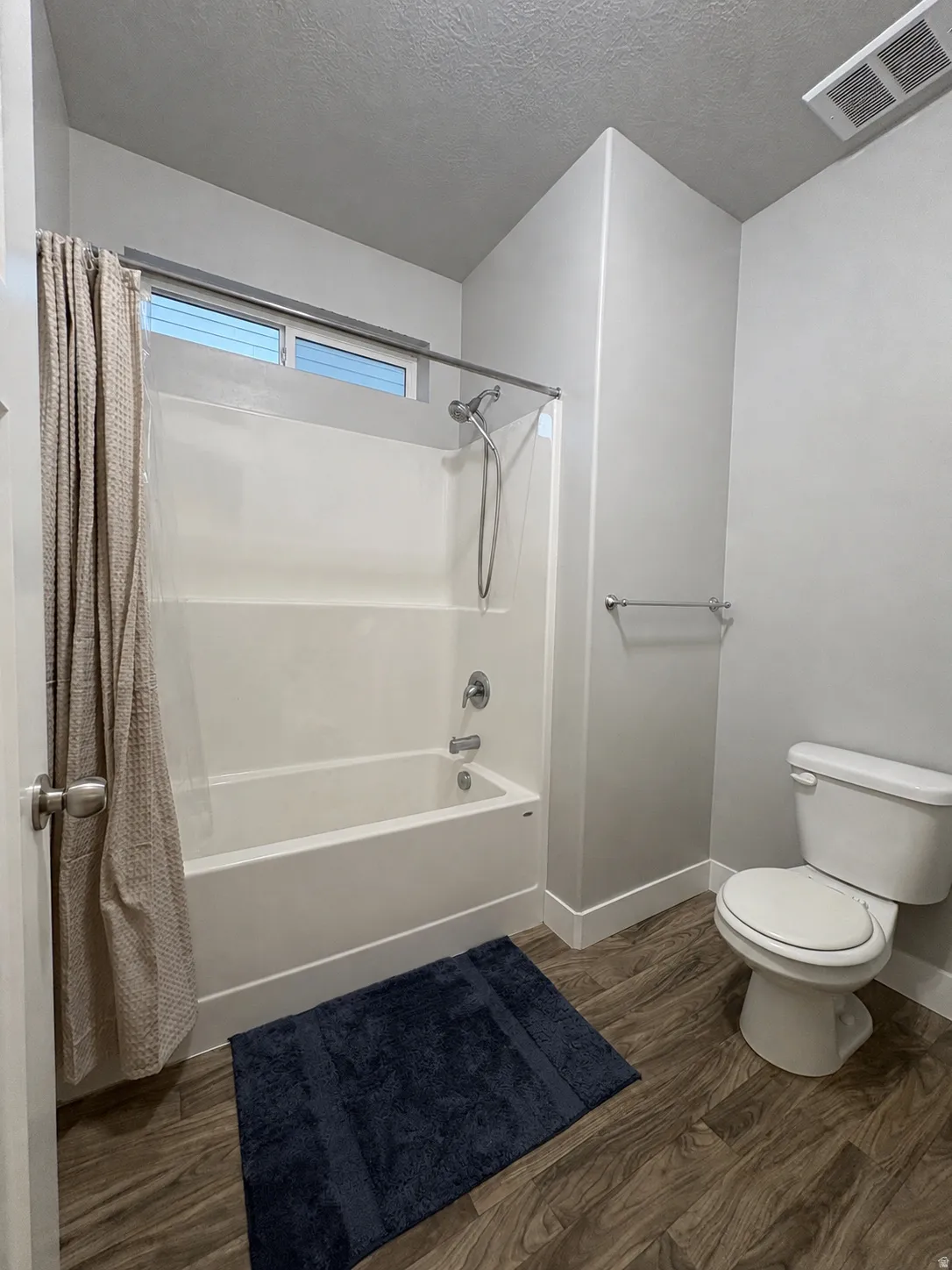 Full bathroom featuring a white tub and shower combination with chrome fixtures, wood-finish flooring, a white toilet, and a window for natural light