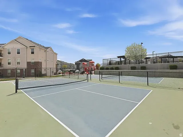 Two outdoor sports courts with perimeter fencing, a distant residential structure with balconies, and a tree with white blossoms