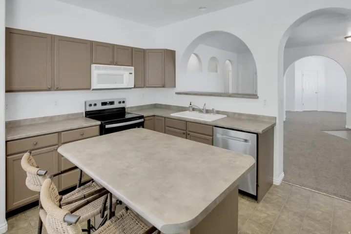Kitchen featuring an eat-at island, perimeter cabinetry, a stainless steel dishwasher, a white built-in microwave, and arched doorways