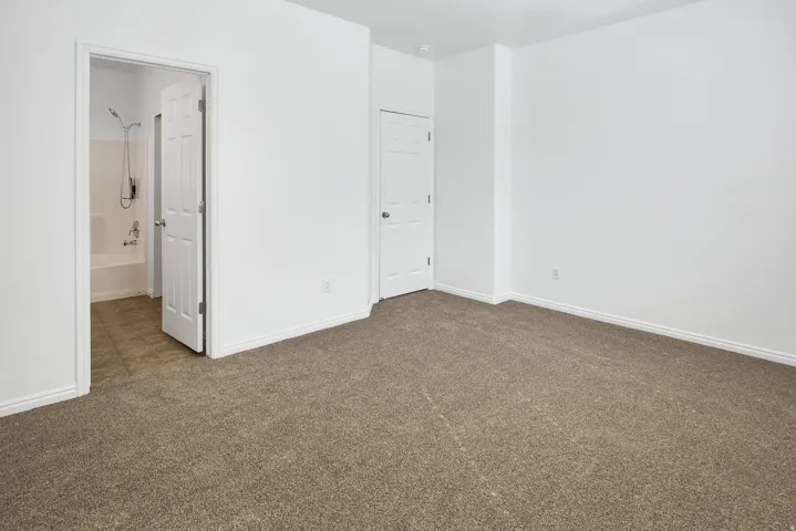 Carpeted flooring, white walls, white trim, interior door, and bathroom access with tiled flooring and a tub/shower combination