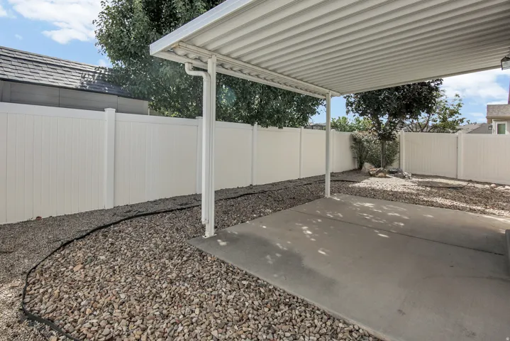 Covered patio with a concrete slab, surrounded by gravel landscaping, and a white privacy fence