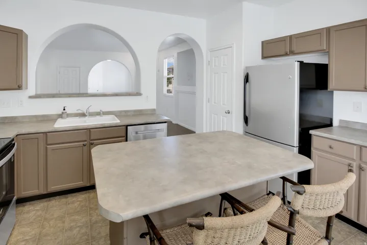 Kitchen featuring neutral cabinetry, a kitchen island, stainless steel appliances, a double basin sink, and arched pass-throughs