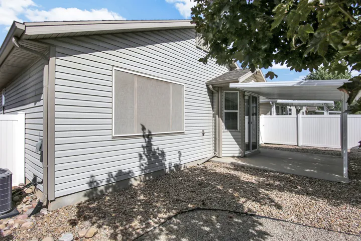 Gray vinyl siding, white privacy fencing, paved patio, and metal carport structure