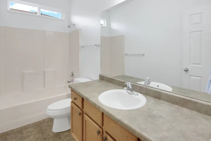 Built-in wood-finish vanity with an integrated sink, a full-width mirror, and a shower-over-tub combination with a tiled surround