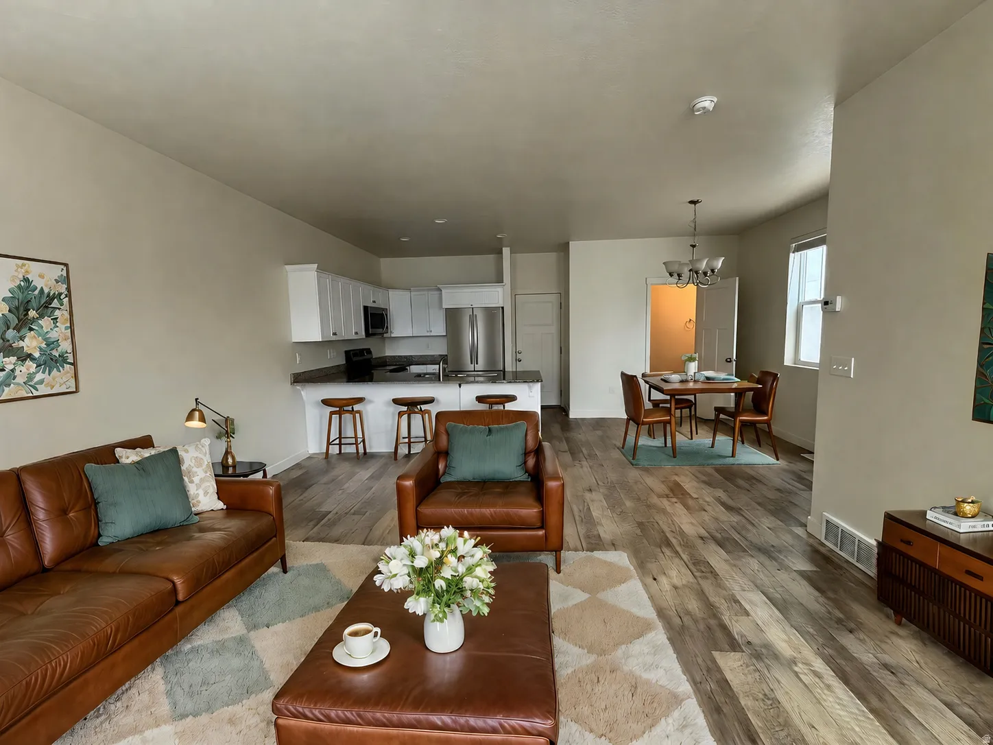 Open-concept living area featuring a cognac leather sofa, wood-finish flooring throughout, and a neutral color palette
