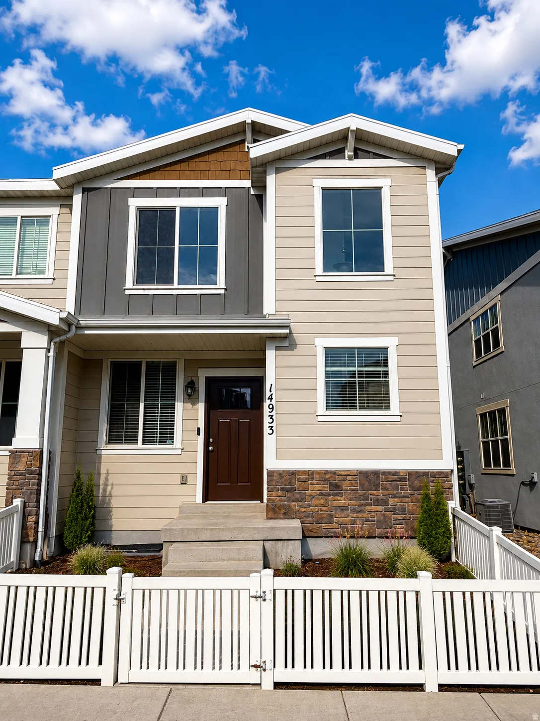 Modern multi-story facade featuring mixed siding, stone accents, and a white picket fence