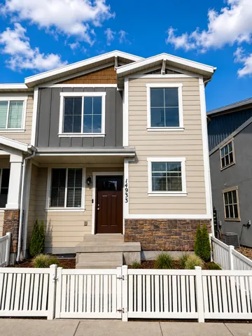 Modern multi-story facade featuring mixed siding, stone accents, and a white picket fence